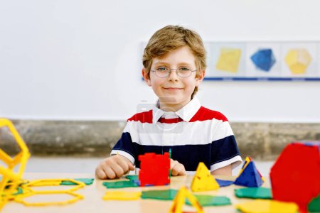 Photo for Little kid boy with glasses playing with lolorful plastic elements kit in school or preschool nursery. Happy child building and creating geometric figures, learning mathematics and geometry - Royalty Free Image