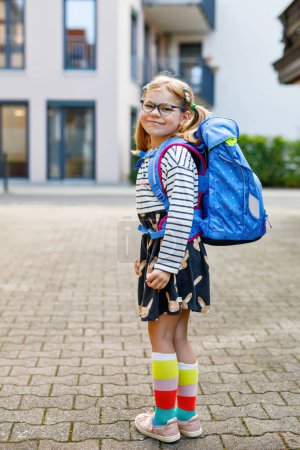 Photo for Cute little girl on her first day going to school. Healthy beautiful child walking to nursery preschool and kindergarten. Happy child with eyeglasses with backpack on the city street, outdoors - Royalty Free Image