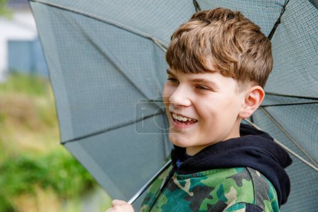 Photo for Portrait of a smiling school boy with rainbow umbrella in the park. Kid walking during rain. Happy positive child. Children activity on bad weather day - Royalty Free Image