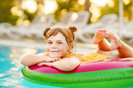 Téléchargez les photos : Bonne petite fille avec flotteur anneau gonflable dans la piscine. Petit enfant d'âge préscolaire apprenant à nager et plonger dans la piscine extérieure de la station hôtelière. Activité sportive saine et plaisir pour les enfants - en image libre de droit