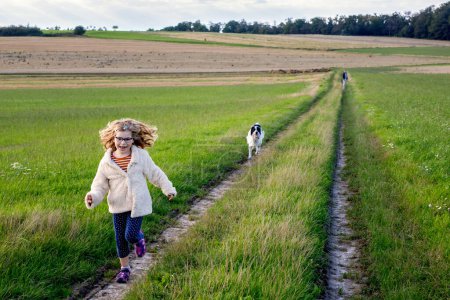 Téléchargez les photos : Petite fille d'âge préscolaire marchant avec son chien. Enfant mignon et animal de compagnie familial dans la nature, les champs et la forêt à la fin de l'été. Amour et amitié entre enfant et chien. S'amuser ensemble - en image libre de droit