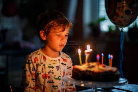 Téléchargez les photos : Adorable petit garçon blond joyeux célébrant son anniversaire. Enfant soufflant sept bougies sur un gâteau fait maison, à l'intérieur. Fête d'anniversaire pour les écoliers, célébration familiale de 7 ans. - en image libre de droit