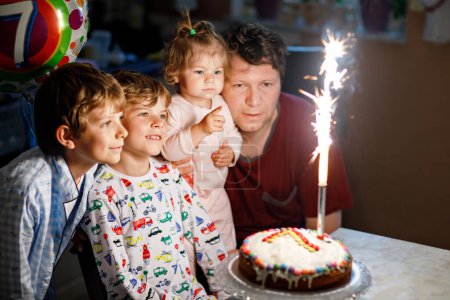Photo for Adorable happy little kid boy celebrating his birthday. Child blowing candles on cake. Father, brother and baby sister sitting together. Happy family - Royalty Free Image