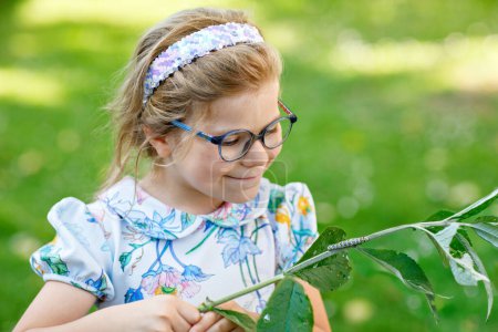 Foto de Pequeña niña preescolar observa oruga subir a la planta. Feliz niño emocionado viendo y aprendiendo insectos en jardines domésticos - Imagen libre de derechos