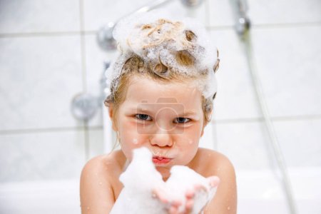 Foto de Lindo niño con espuma de champú y burbujas en el baño de toma de pelo. Retrato del feliz concepto de salud e higiene de la niña preescolar sonriente. Lava el cabello por sí misma - Imagen libre de derechos
