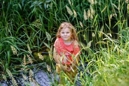 Téléchargez les photos : Une fille heureuse embrasse les joies de l'enfance alors qu'elle explore un ruisseau estival, s'immergeant dans des merveilles naturelles et des découvertes ludiques. Enfant d'âge préscolaire et été - en image libre de droit