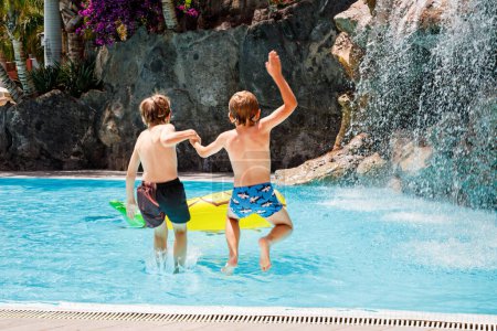Téléchargez les photos : Deux petits garçons heureux sautant dans la piscine et s'amusant en vacances en famille dans une station hôtelière. Enfants en bonne santé, frères et sœurs et meilleurs amis jouant dans l'eau
. - en image libre de droit