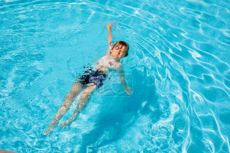 Téléchargez les photos : Portrait de petit garçon heureux dans la piscine et s'amuser en vacances en famille dans une station hôtelière. Enfants en bonne santé jouant dans l'eau, nageant et éclaboussant - en image libre de droit