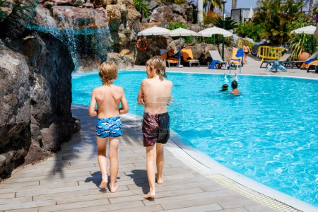 Photo for Two happy little kids boys jumping in the pool and having fun on family vacations in a hotel resort. Healthy children, siblings and best friends playing in water. - Royalty Free Image