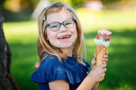 Photo for Happy preschool girl eating colorful ice cream in waffle cone on sunny summer day. Little toddler child eat icecream dessert. Sweet food on hot warm summertime days. Bright light, colorful ice-cream - Royalty Free Image