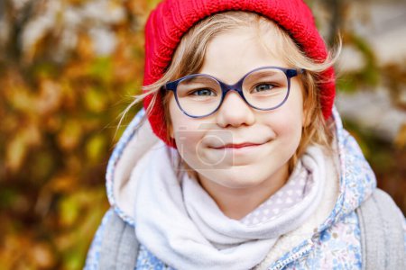 Photo for Portrait of a cute preschool girl with eye glasses and red hat outdoors. Happy funny child wearing new blue glasses. Autumn day in the city - Royalty Free Image