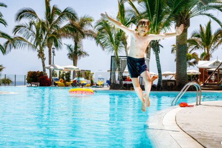 Photo for Happy little kid boy jumping in the pool and having fun on family vacations in a hotel resort. Healthy child playing in water - Royalty Free Image