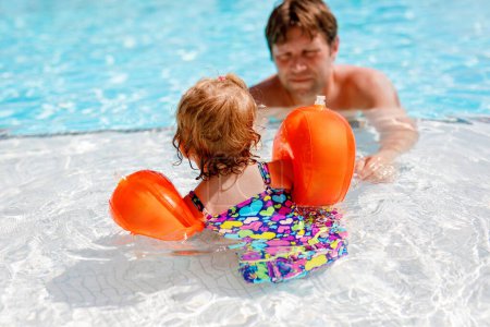 Photo for Cute happy little toddler girl and father in the pool and having fun on family vacations in a hotel resort. Healthy child and man playing in water. Baby daughter in colorful fashion swimsuit - Royalty Free Image