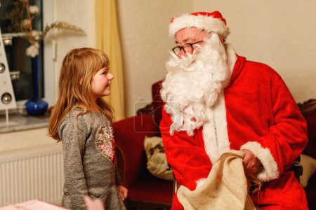Foto de Niña pequeña hablando con Santa Claus llamada Nikolaus o Weihnachtsmann en alemán. Feliz niño sonriente esperando regalos. Santa con libro de oro. Navidad, infancia, vacaciones. - Imagen libre de derechos