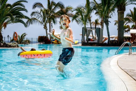 Téléchargez les photos : Joyeux petit garçon sautant dans la piscine et s'amusant en vacances en famille dans une station hôtelière. Enfant sain jouant dans l'eau - en image libre de droit