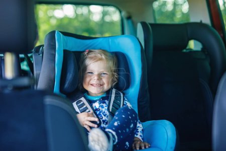 Photo for Adorable baby girl with blue eyes sitting in car safety seat. Toddler child going on family vacations and jorney. Smiling happy child during traffic jam - Royalty Free Image