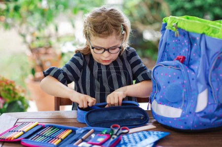 Photo for Happy smiling girl preparing for school her backpack. First day of school. Back to school concept. Little child collecting different supplies like pens and books in a bag or satchel - Royalty Free Image