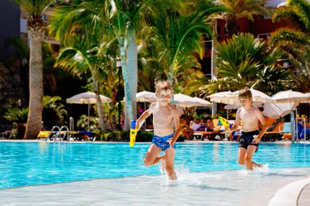 Photo for Two happy little kid boys jumping in the pool and having fun on family vacations in a hotel resort. Children playing in water with a water gun. Laughing running siblings brothers and best friends. - Royalty Free Image
