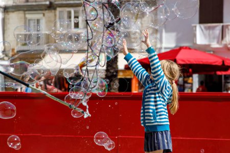 Téléchargez les photos : Petite fille jouant dans la rue avec des bulles de savon soufflant. Joyeux enfant dans la ville - en image libre de droit