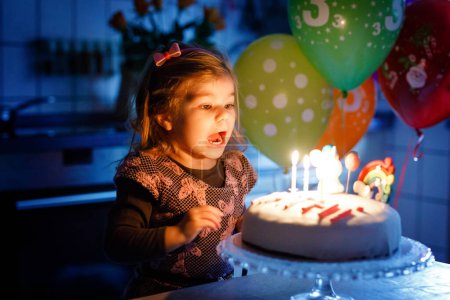 Photo for Adorable little toddler girl celebrating third birthday. Baby toddler child with homemade unicorn cake, indoor. Happy healthy toddler is suprised about firework sparkler and blowing candles on cake. - Royalty Free Image