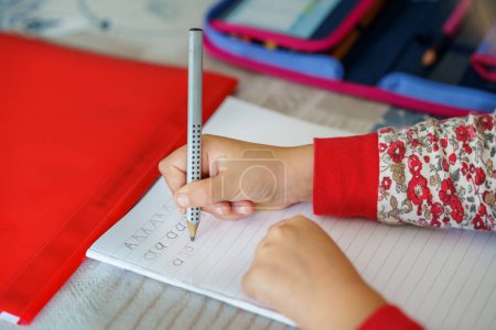 Téléchargez les photos : Petite fille faisant ses devoirs. Gros plan de la main avec crayon apprenant à écrire des lettres. Lettre d'écriture pour enfant A. Premiers jours d'école - en image libre de droit