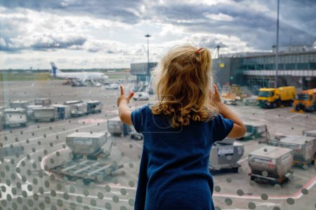 Foto de Linda niñita en el aeropuerto, viajando. Feliz niño sano esperando cerca de la ventana y viendo aviones. Familia de vacaciones de verano en avión - Imagen libre de derechos