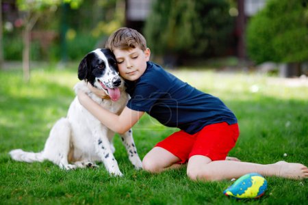 Photo for Active kid boy playing with family dog in garden. Laughing school child having fun with training dog, running and playing with ball. Happy family outdoors. Friendship between animal and kids. - Royalty Free Image