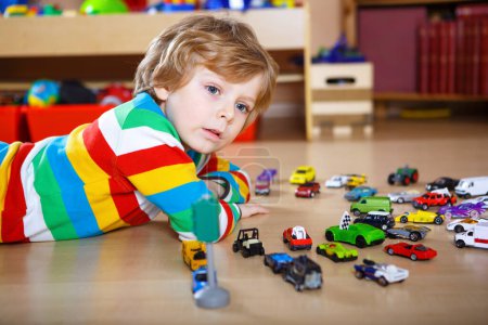 Photo for Lovely blond kid boy playing with lots of toy cars indoor. Happy healthy child boy having fun during pandemic coronavirus quarantine disease. Child alone at home, closed nursery - Royalty Free Image