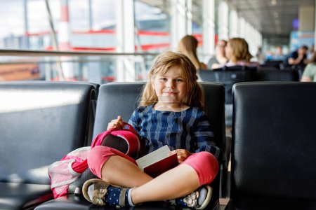 Téléchargez les photos : Petite fille à l'aéroport attendant l'embarquement à la grande fenêtre. Enfant mignon tenant passeport.. J'ai hâte de partir pour des vacances d'été en famille. - en image libre de droit