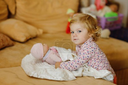 Photo for Adorable cute little toddler girl playing with doll. Happy healthy baby child having fun with role game, playing mother at home or nursery. Active daughter with toy - Royalty Free Image