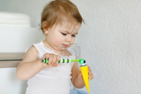 Foto de Niña sosteniendo cepillo de dientes y cepillándose los primeros dientes. Niño aprendiendo a limpiar los dientes de leche. Concepto de prevención, higiene y salud. Niño feliz en el baño. - Imagen libre de derechos
