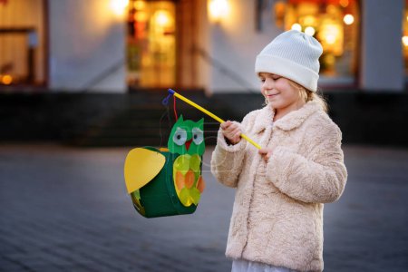 Photo for Little preschool kid girl holding selfmade traditional owl lanterns with candle for St. Martin procession. child happy about children and family parade in kindergarten. German tradition Martinsumzug. - Royalty Free Image