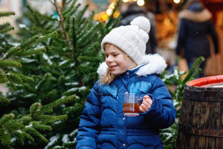 Photo for Little cute preschool girl drinking hot children punch or chocolate on German Christmas market. Happy child on traditional family market in Germany, Laughing boy in colorful winter clothes. - Royalty Free Image