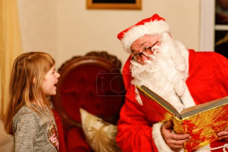 Téléchargez les photos : Petite fille tout-petit parlant au Père Noël appelé Nikolaus ou Weihnachtsmann en allemand. Joyeux enfant souriant attendant des cadeaux. Père Noël avec livre d'or. Noël, enfance, vacances. - en image libre de droit