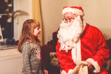 Téléchargez les photos : Petite fille tout-petit parlant au Père Noël appelé Nikolaus ou Weihnachtsmann en allemand. Joyeux enfant souriant attendant des cadeaux. Père Noël avec livre d'or. Noël, enfance, vacances. - en image libre de droit