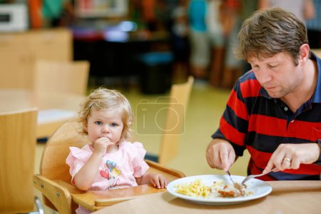 Photo for Toddler girl eating healthy vegetables and unhealthy french fries potatoes. Cute happy baby child taking food from parents dish in restaurant. Father eating in fast food restaurant with daughter. - Royalty Free Image