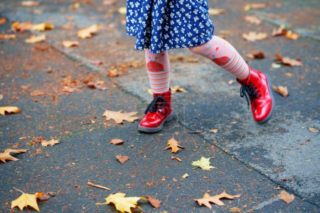 Téléchargez les photos : Petite fille marchant dans des chaussures rouges dans le parc d'automne. Gros plan des jambes des enfants en chaussures dansant et marchant à travers les feuilles et le feuillage automnaux d'automne. - en image libre de droit