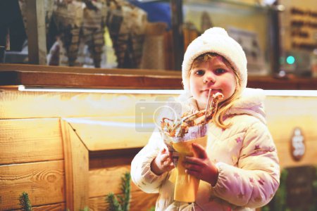 Photo for Little preschool girl, cute child eating churros sweets covered with chocolate with decoration and lights on background. Happy child on Christmas market in Germany - Royalty Free Image