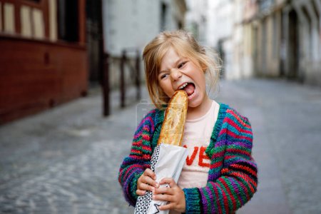Photo for Adorable little preschool girl with fresh French baguette on the street side of the city. Happy small child in Paris, France - Royalty Free Image