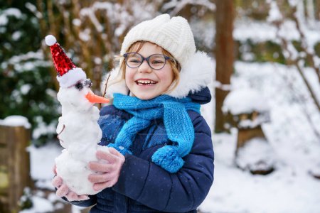 Photo for Cute little preschool girl with glasses making mini snowman. Adorable healthy happy child playing and having fun with snow, outdoors on cold day. Active leisure with children in winter. - Royalty Free Image