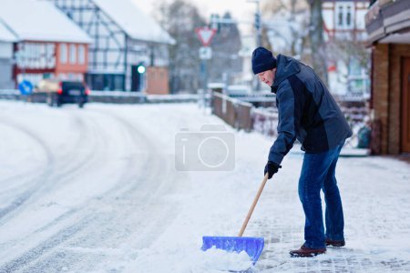 Photo for Man with snow shovel cleans sidewalks in winter during snowfall. Winter time in Europe. Young man in warm winter clothes. Snow and weather chaos in Germany. Snowstorm and heavy snowing. Schneechaos. - Royalty Free Image