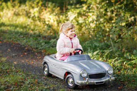 Photo for Little preschool girl driving big vintage toy car. Happy child having fun with playing outdoors. Active preschooler child enjoying warm autumn day in forest. Smiling stunning kid playing. - Royalty Free Image