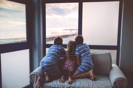 Foto de Tres niños mirando el amanecer en la terraza o balcón. Dos chicos y una niña en edad preescolar ven el sol en el horizonte. Niños felices relajándose cerca de la playa, familia disfrutando de una hermosa vista - Imagen libre de derechos