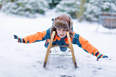Photo for Little kid boy enjoying sleigh ride during snowfall. Happy preschool kid riding on vintage sledge. Child play outdoors with snow. Active fun for family Christmas vacation in winter. - Royalty Free Image