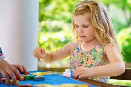 Foto de Little preschool girl playing board game with colorful bricks. Happy child build tower of wooden blocks, developing fine motor skills, home joint games. Leisure activities for children at home - Imagen libre de derechos