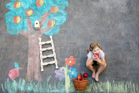 Photo for Cute little girl painting with colorful chalks apples harvest from apple tree on asphalt. Cute preschool child with having fun with chalk picture. Creative leisure for children, drawing and painting - Royalty Free Image