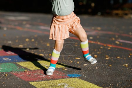 Foto de Primer plano de las piernas de la niña jugando hopscotch juego dibujado con tiza de colores sobre asfalto. Pequeño niño activo saltando en el patio al aire libre en un día soleado. Actividades de verano para niños - Imagen libre de derechos