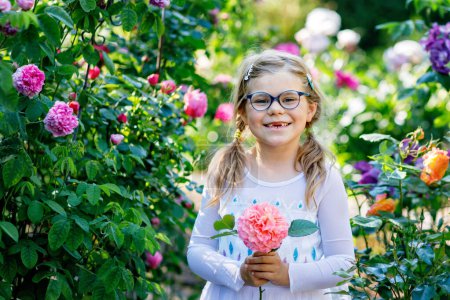Photo for Cute adorable little preschool girl rose flower and princess dress in garden.. Portrait of smiling preschool child in domestic garden on warm spring or summer day. Summertime - Royalty Free Image