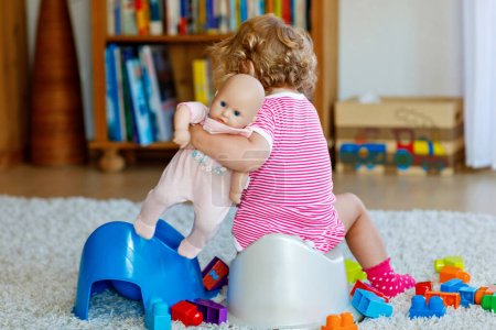 Foto de Primer plano de un niño pequeño y lindo de 12 meses sentado en el orinal. Niño jugando con muñeco de juguete. Concepto de entrenamiento de baño. Aprendizaje del bebé, pasos de desarrollo. - Imagen libre de derechos