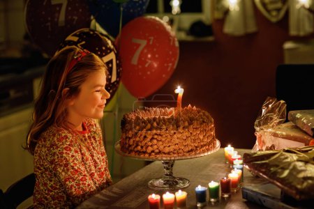 Téléchargez les photos : Joyeux anniversaire de petite fille. Mignon enfant souriant avec gâteau princesse fait maison, intérieur. Heureux enfant préscolaire sain soufflant sept bougies sur le gâteau. - en image libre de droit